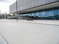 a white parking lot with an empty bench sitting on top of it and a large building behind it