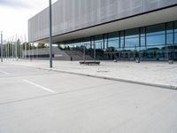 a white parking lot with an empty bench sitting on top of it and a large building behind it