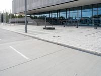 a white parking lot with an empty bench sitting on top of it and a large building behind it