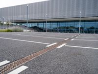 an empty car park at the entrance of a large building with multiple windows and two bars across the street from the parking area