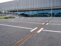 an empty car park at the entrance of a large building with multiple windows and two bars across the street from the parking area