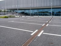 an empty car park at the entrance of a large building with multiple windows and two bars across the street from the parking area