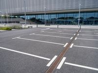 an empty car park at the entrance of a large building with multiple windows and two bars across the street from the parking area