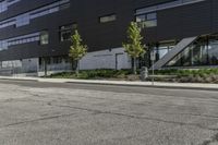 a parking lot next to a tall black building and some trees on it's side