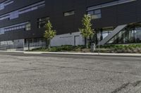 a parking lot next to a tall black building and some trees on it's side