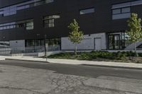 a parking lot next to a tall black building and some trees on it's side