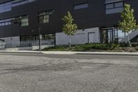 a parking lot next to a tall black building and some trees on it's side