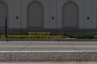 a fire hydrant standing next to a curb near a building and bushes and grass