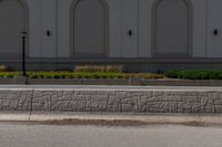 a fire hydrant standing next to a curb near a building and bushes and grass