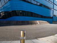 a fire hydrant sitting next to a large blue building by the sidewalk in front of a building