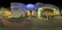 a spherical photograph of a building at night with lights around it and people on the sidewalk