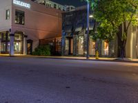 a city street has buildings at night and some trees in the foreground on one side