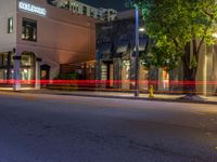 a city street has buildings at night and some trees in the foreground on one side