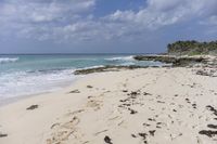 a beach has many footprints and rocks, sand, and clear water as well as waves