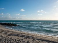 the sun is shining over the ocean and beach with a sandy shoreline along it and a person holding a surfboard