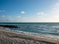 the sun is shining over the ocean and beach with a sandy shoreline along it and a person holding a surfboard