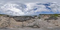 the view through the fisheye lens of the ocean from a beach area of a stone formation