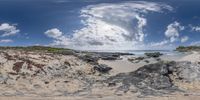 a panoramic view looking at the beach and sea with clouds overhead in an almost clear image