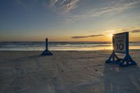 two blue posts sit on the sand at sunset beside the ocean's edge with speed limit sign