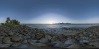 a city skyline and a rocky beach at sunset in the middle of the ocean and a wall of rocks with water in front of the ground