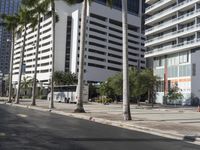 an empty city sidewalk surrounded by tall buildings and trees in a city square with cars and pedestrians passing on the road