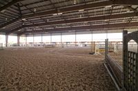 an indoor riding gym with some horses inside of it and a few stalls to the right