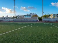 empty football stadium with green grass and bleachers at sunset and high rise buildings