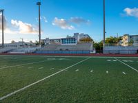 empty football stadium with green grass and bleachers at sunset and high rise buildings