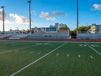 empty football stadium with green grass and bleachers at sunset and high rise buildings