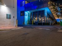 an empty city street with lit lights in front of a store at night with blue and yellow