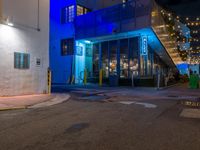 an empty city street with lit lights in front of a store at night with blue and yellow