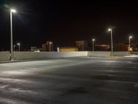 a deserted empty parking lot at night time with street lights illuminating in the distance over buildings