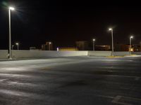 a deserted empty parking lot at night time with street lights illuminating in the distance over buildings