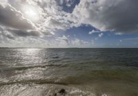 the sun is shining brightly over the water at the beach while clouds float overhead above