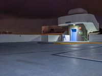 a building with parking spaces underneath it at night with purple skies behind the sky and a door in between two