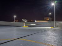 an empty parking lot near a city at night with buildings in the background and a yellow arrow indicating the corner