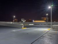 an empty parking lot near a city at night with buildings in the background and a yellow arrow indicating the corner