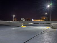 an empty parking lot near a city at night with buildings in the background and a yellow arrow indicating the corner