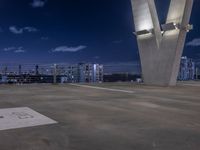 a concrete area with large white and blue buildings in the background at night and a city sky