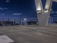 a concrete area with large white and blue buildings in the background at night and a city sky