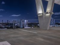 a concrete area with large white and blue buildings in the background at night and a city sky