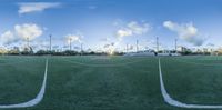 there is a green soccer field near the houses and clouds in the sky from a point of view