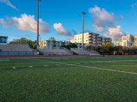 empty soccer field with housing apartments in the background, under a blue sky and a white stripe