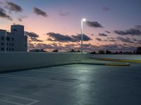 a parking lot with a building in the background and street lamps lite up at dusk