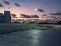 a parking lot with a building in the background and street lamps lite up at dusk