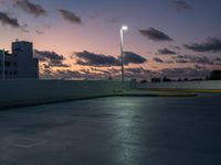 a parking lot with a building in the background and street lamps lite up at dusk