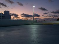 a parking lot with a building in the background and street lamps lite up at dusk