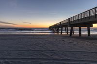 a long pier that extends into the ocean at sunset is seen along this beachfront