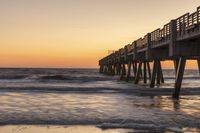 a wooden pier is shown as the sun sets over the ocean and waves are just around