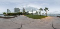 a park with an area with grass, buildings and trees in it, near water